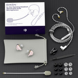 A BASN in-ear gaming headset wired with dual microphones, shown with its retail box and laid out accessories on a dark textured background. The set includes a silver braided cable, two pink-and-silver in-ear earpieces, a gray carrying pouch, ear tips in black and white, a small cleaning tool, and a clip.